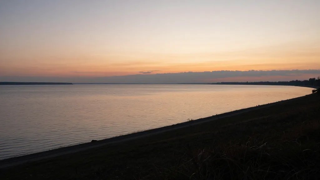 Quiet lakeside ridge at sunset, distant horizon glow over water