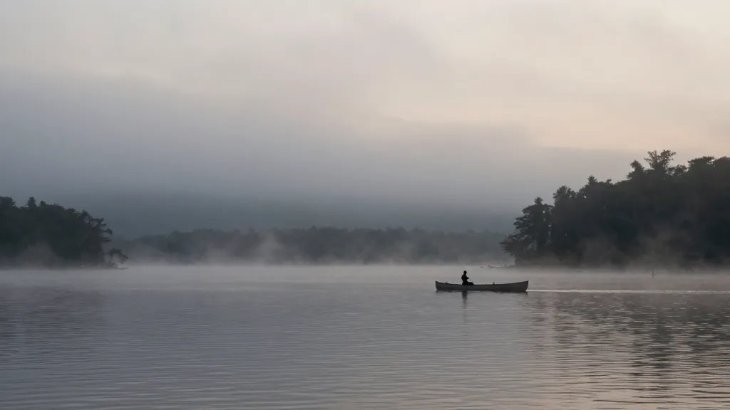 Vast shoreline of Misty Lake at dawn, lone canoe silhouette on misty water