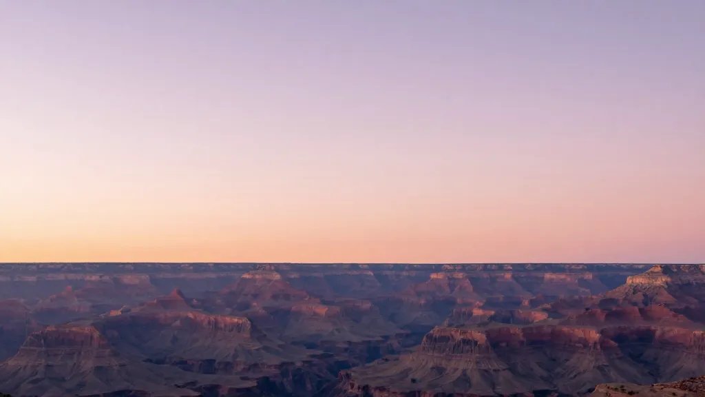 Soft pink to gold dawn over a distant canyon rim, solitary horizon line