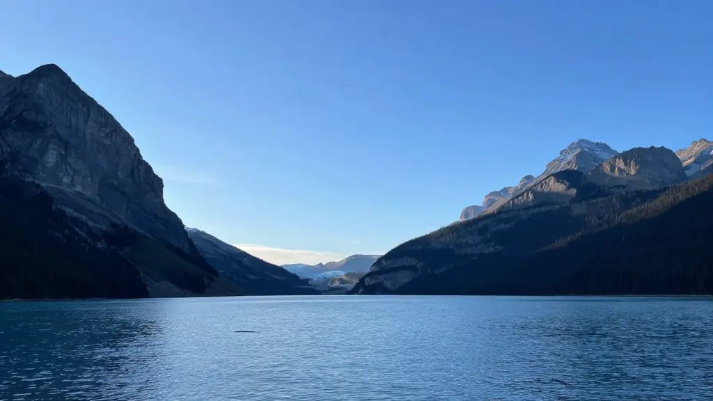 Distant view of Lake Louise shoreline under clear blue sky, minute glacier silhouettes