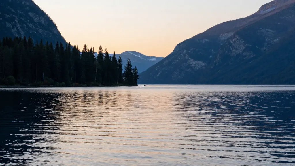 Distant sunrise over Lake Crescent's glassy water with evergreen shoreline